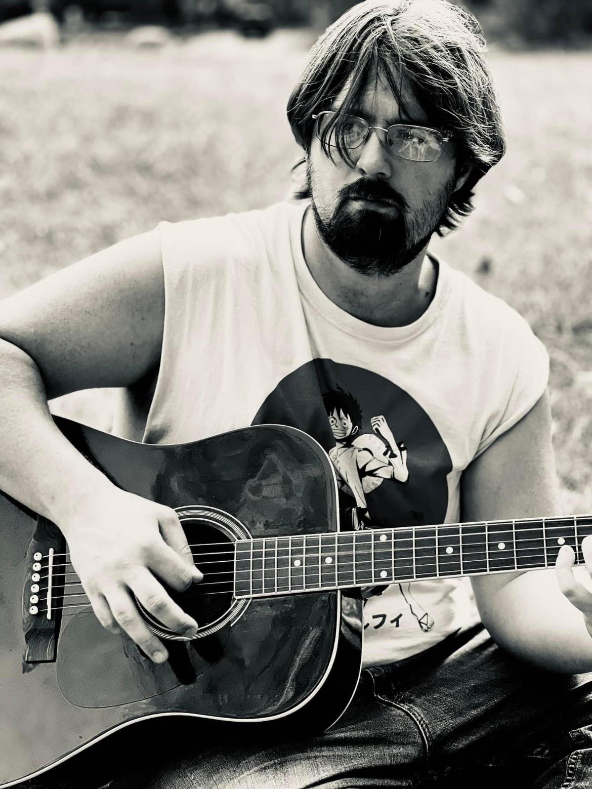 The music instructor cameron sitting at ledges state park playing guitar.